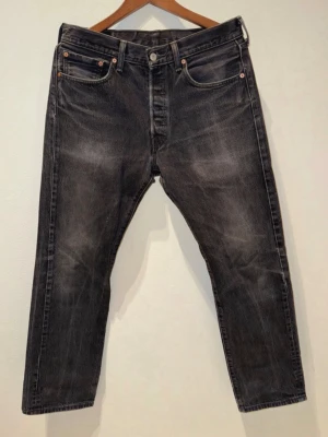 Svarta Levi's jeans  - Säljer ett par svarta jeans från Levi's med klassisk femficksdesign och raka ben. Jeansen har en snygg tvättad look och är tillverkade i slitstark denim. Perfekt för dig som gillar en tidlös och cool stil. Strl 33/32 sitter som 30/32