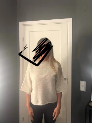 Ljusgrå stickad tröja med vida ärmar - Ljusgrå stickad tröja med rund hals och vida, trekvartsärmar. Tröjan har en avslappnad passform och är gjord i ett mjukt material som passar perfekt för lager-på-lager. Enkel och stilren design utan synliga loggor eller mönster.