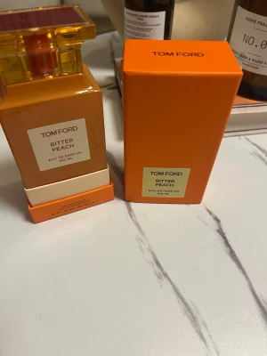 Tom Ford Bitter Peach Eau de Parfum - HELT FULL!!!!Tom Ford Bitter Peach Eau de Parfum i en lyxig orange glasflaska med guld- och röda detaljer. Flaskan har en fyrkantig form och kommer med matchande orange kartong. Doften är fruktig och exklusiv, perfekt för dig som vill sticka ut.