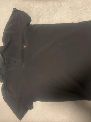 Svart piké från GANT - Snygg svart piké från GANT med klassisk krage och knappar framtill. Skjortan har diskret broderad logga på bröstet och är tillverkad i ett mjukt bomullsmaterial. Perfekt för en stilren och avslappnad look.