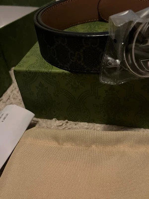 Svart GG-bälte från Gucci i skinn - Snyggt svart bälte från Gucci med klassiskt GG-mönster och stor silverfärgad logospänne. Bältet är gjort i skinn och har en lyxig känsla, perfekt för att lyfta vilken outfit som helst.