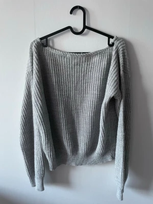 Ljusgrå stickad tröja - En enkel och stilren ljusgrå stickad tröja med bred halsringning och långa ärmar. Tröjan har en grovstickad struktur och ribbade muddar vid ärmslut och nederkant. Perfekt att slänga på sig över ett linne eller t-shirt.
