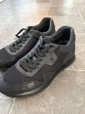 Svarta Louis Vuitton sneakers mesh/läder - Behöver torkas av. Och något slitet på kanten som inte syns när man har på sig dom. I annat så är dom i bra skick och skit fina! Billig pris pga det lilla slitna. Se bilder. Snygga helsvarta sneakers från Louis Vuitton med LV-logga på sidan och detaljer i både mesh och läder. Skorna har svarta skosnören, diskreta monogramdetaljer på sulan och en sportig, låg siluett. Perfekta för dig som gillar exklusiv streetwear.