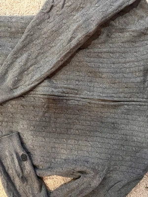 Grå kabelstickad tröja Cutter & Buck, M - Snygg grå kabelstickad tröja från Cutter&Buck  med diskret logomärke på ärmen. Tröjan har ribbade muddar och ett klassiskt mönster som ger en stilren look. Perfekt för dig som gillar enkel men trendig stil. Dragkedja, herr M, 100% bomull