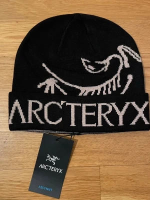 Arc’teryx Ascent Beanie – Svart – Oanvänd! - Snygg svart mössa från Arc'teryx med stor vit logga och text framtill. Klassisk uppvikt kant och stickad i mjukt material som passar perfekt till kalla dagar. Perfekt accessoar för dig som gillar outdoor och streetwear.