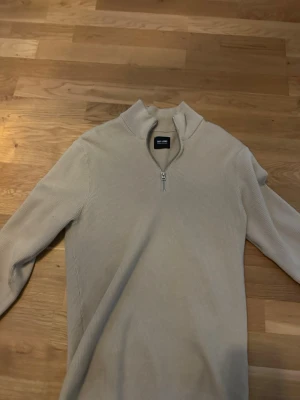 Beige stickad tröja med halv dragkedja - Säljer en stilren beige stickad tröja från only sons. Tröjan har en hög krage med halv dragkedja och är ribbstickad för en snygg struktur. Perfekt för lager på lager och enkel att matcha med olika outfits.