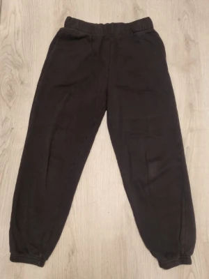 Svarta mjukisbyxor från H&M - Ett par svarta mjukisbyxor från H&M med resår i midjan och vid bensluten. Byxorna är tillverkade i mjukt och bekvämt material, perfekta för chill dagar. Klassisk rak passform och enkel design utan tryck eller detaljer.