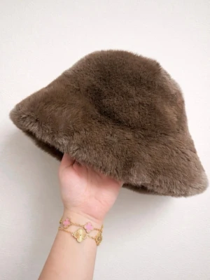 Brun fluffig bucket hat - Säljer en brun bucket hat i supermjuk fuskpäls. Hatten har en klassisk rund form och bredare brätte som ger en cool och trendig look. Perfekt accessoar för att lyfta din outfit under kyligare dagar.