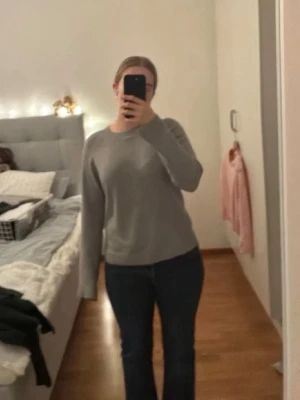 Grå stickad tröja - Enkel och stilren grå stickad tröja med rund halsringning och långa ärmar. Tröjan har ribbstickade muddar vid ärmslut och nederkant. Perfekt att matcha med jeans eller kjol för en avslappnad look.