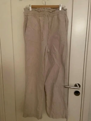 Beige linnebyxor från Cubus  - Luftiga beige linnebyxor från Cubus med resår och dragsko i midjan. Byxorna har raka ben och sidofickor, perfekta för en avslappnad och stilren look. Tillverkade i ett svalt linnematerial som passar perfekt till sommaren.