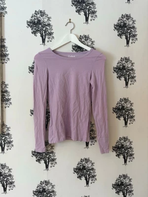 Ljuslila långärmad topp Cubus - Säljer en ljuslila långärmad topp från Cubus med rund halsringning. Modellen är figurnära och enkel i designen, perfekt att matcha med jeans eller kjol. Tillverkad i mjukt och stretchigt material för en bekväm känsla.