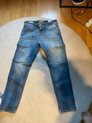 Blå tapered jeans från Jack & Jones 28 32 - Snygga blå jeans från Jack & Jones i modellen Tapered/Mike. Jeansen har klassisk femficksdesign, normalhög midja och avsmalnande ben. Tillverkade i slitstarkt denim med snygga slitningar och kontrastsömmar.