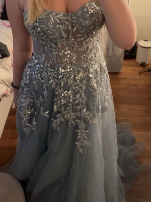 Blå balklänning - Säljer min balklänning från förra året. Den är använd en gång. Det är en lång ljusblåklänning med  tunna axelband som går att ta av. Klänningen har ett silvrigt paljett blommönster och knyt snören baktill. Ord pris är 2000 men säljer för 1500. Hör gärna av er om ni har några frågor     