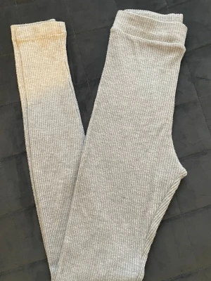Ljusgrå ribbade leggings - Säljer ett par ljusgrå leggings med ribbad struktur. De är stretchiga och mjuka, perfekta för en chill och avslappnad stil samtidigt som man vill känna sig fin och fräsch. Super skönt och mjukt material. 