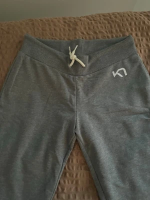 Grå mjukisbyxor från Kari Traa - Snygga grå mjukisbyxor från Kari Traa med bred mudd i midjan och vit dragsko. Byxorna har en avslappnad passform och är tillverkade i mjukt material, perfekta för chill dagar. Diskret logga på höften för en clean look.