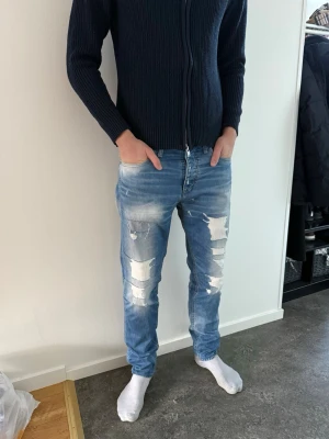 Blå slitna jeans med patchdetaljer - Säljer ett par ljusblå jeans med slitningar och patchdetaljer på framsidan. Jeansen har skinny fit och klassisk femficksmodell. Snygg tvätt med både slitna och lagade partier som ger en trendig look. Perfekta för dig som gillar streetstyle och vill sticka ut. W31 L34