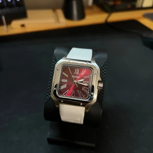 Seiko fyrkantig klocka vit/silver - Stilren fyrkantig klocka från Seiko med vit läderrem och boett i silverfärgad metall. Urtavlan är svart med röda detaljer och romerska siffror. Mekaniskt urverk NH35 som syns genom baksidan. Perfekt för dig som gillar unika accessoarer. 