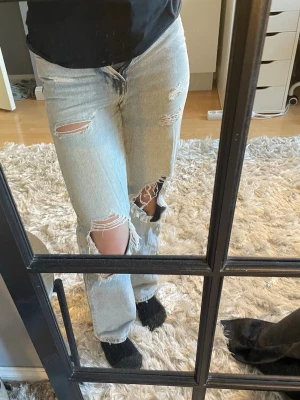 Ljusa blåa jeans med hål i - Säljer ett par ljusblå jeans med hål vid knäna och låren. Jeansen har en avslappnad passform och raka ben. Perfekta för en trendig och avslappnad stil. Materialet är klassisk denim i bomull. Hålen och slitage är mode köpes sådär. Ej använt på länge men det är fina tycker jag. Ej bra pris,,, skriv till mig