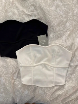 Black & white top from H&M - Två bustiers från H&M i svart och vitt. De har en snygg, figurnära passform med markerade sömmar och lätt vadderad byst. Materialet är stretchigt och består av polyester. Perfekta att styla under skjortor eller som de är.