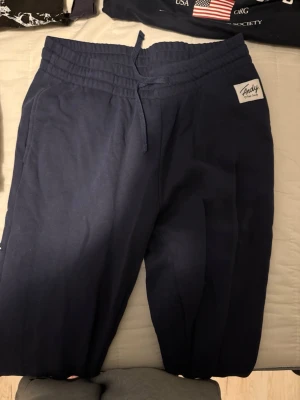 Mörkblå mjukisbyxor Frank Dandy - Mörkblå mjukisbyxor från Frank Dandy med dragsko i midjan och resår. Byxorna har en enkel och clean look med en liten logga på höften. Perfekta för chill dagar eller när du vill vara bekväm. Tillverkade i mjukt material som känns skönt mot huden.