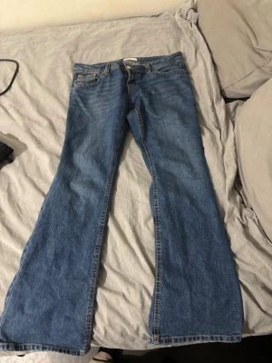 Blå bootcut jeans med låg midja - Säljer ett par klassiska blå bootcut jeans med låg midja och fem fickor. Jeansen har orangea sömmar och bälteshällor. Materialet är denim i bomull och passformen är utsvängd nedtill. Och är i storlek 38 från Gina tricot 