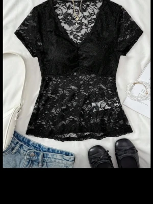 Svart spetsblus med v-ringning - Snygg svart blus i genombruten spets med v-ringad hals och korta ärmar. Modellen är lätt utsvängd och ger en feminin siluett. Perfekt att styla med jeans eller kjol för en trendig look. Säljer då den inte används ❤️