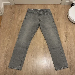 Grå raka jeans från jack&jones - Snygga grå jeans från jack&jones med klassisk femficksdesign och raka ben. Jeansen har en cool tvättad look och är tillverkade i robust denim. Perfekta för dig som gillar en stilren och avslappnad vibe.