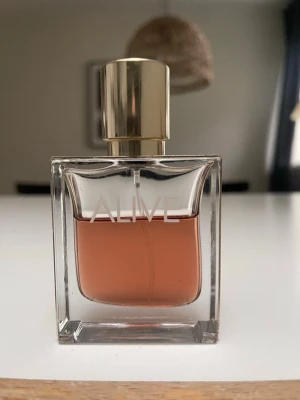 Hugo Boss Alive Eau de Parfum - Snygg parfymflaska från Hugo Boss med namnet ALIVE. Flaskan är rektangulär i genomskinligt glas med guldigt lock och detaljer. Innehållet har en varm, bärnstensfärgad ton som ger en lyxig känsla. Perfekt för dig som vill ha en elegant och modern doft i samlingen.