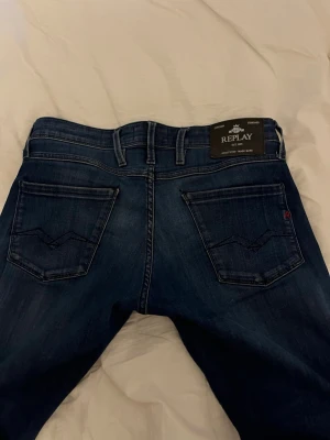 Replay blå jeans straight fit - Snygga blå jeans från Replay med klassisk femficksdesign och raka ben. Jeansen har en mörk tvätt med lätt slitning och kontrastsömmar. Passar dig som gillar en stilren look med bekväm passform. Materialet är mjukt jeans och midjan är normal.