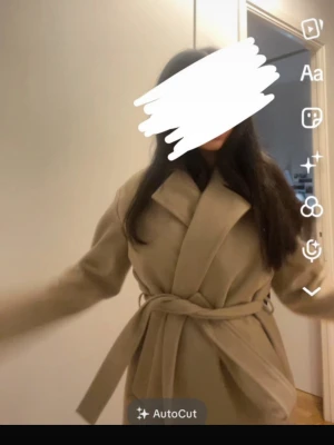 Beige kappa med knytskärp - Stilren beige kappa med bred krage och knytskärp i midjan. Kappan har en rak passform och är tillverkad i ett mjukt tyg som ger en elegant look. Perfekt för dig som vill ha en klassisk och trendig ytterjacka.