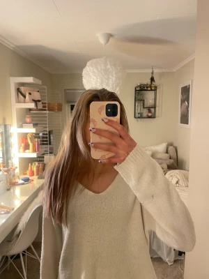 Vit stickad tröja med v-ringning - Mysig vit stickad tröja med djup v-ringning och långa ärmar. Tröjan har en avslappnad passform och är perfekt för lager på lager. Passar till både jeans och kjol för en chill look.