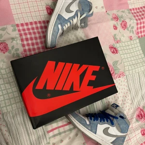 Nike Air Jordan 1 High Hyper Royal - Nike Air Jordan 1 High Hyper Royal med vit och ljusblå mocka, grå swoosh och vita samt blå skosnören. Klassisk high-top siluett med perforerad tå och ikonisk Air Jordan-logga på sidan. Skorna har en fräsch vibe och passar perfekt till streetwear. (Äkta)