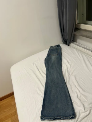 Blå bootcut jeans med slitningar - Säljer ett par blå bootcut jeans med lätt slitna detaljer och klassisk femficksdesign. Jeansen har normal midja och vida ben som ger en retrovibe. Perfekta till sneakers eller boots för en avslappnad look.