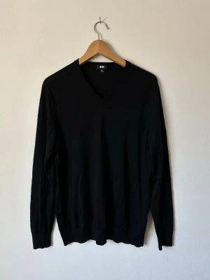Svart stickad tröja från Uniqlo - Klassisk svart stickad tröja från Uniqlo med V-ringning och långa ärmar. Tröjan har en enkel och stilren design med ribbade muddar vid ärmslut och nederkant. Perfekt basplagg för lager på lager och funkar året runt. 8D9