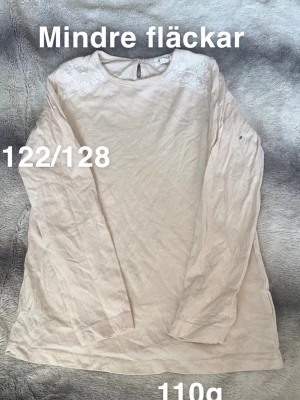  långärmad topp med spets - Söt långärmad topp med rund hals och spetsdetaljer på axlarna. passar perfekt till vardags eller när du vill vara extra fin. Knäppning bak i nacken för enkel påklädning.🌸Mindre fläckar. Färg: något mellan beige och aprikos. Storlek 122/128  
