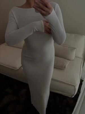 Vit långärmad långklänning - Säljer en stilren vit långklänning med långa ärmar och rund halsringning. Klänningen har en kroppsnära passform och är tillverkad i ett mjukt, stretchigt material som ger en snygg siluett.