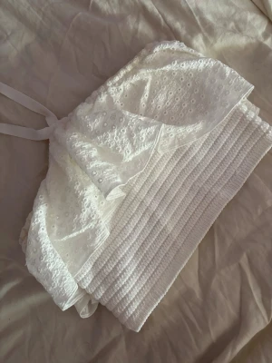 Vit broderad bandeau topp med volang - Supersöt vit bandeau topp från Zara med broderade detaljer och volang. Toppen har smockad nederdel och knytband i nacken för en snygg passform. Perfekt för sommarens alla tillfällen och ger en romantisk vibe.