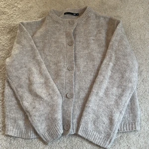 Beige stickad kofta från lager 157 - Mysig beige stickad kofta med rund halsringning och stora matchande knappar framtill. Koftan har långa ärmar och ribbade muddar vid ärmslut och nederkant. Använd en enstaka gång 