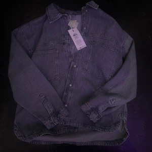 Oversized grå jeansjacka - Säljer en oversized grå jeansjacka med två stora bröstfickor och klassisk krage. Jackan har knäppning framtill och långa ärmar med knapp vid ärmslut. Perfekt för en avslappnad och trendig look.  Helt ny med lapp, nypris 699