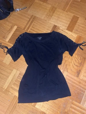 Svart topp med snörning på ärmar - Snygg svart topp med korta ärmar och cool snörningsdetalj längs ärmarnaPerfekt för dig som gillar en enkel men trendig stil. 