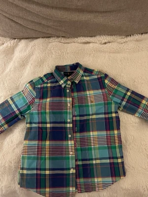 Rutig skjorta från Ralph Lauren - Färgglad rutig skjorta från Ralph Lauren med klassisk krage och knappar framtill. Skjortan har inslag av blått, grönt, gult och rött samt den ikoniska broderade loggan på bröstet. Perfekt för dig som gillar preppy stil.