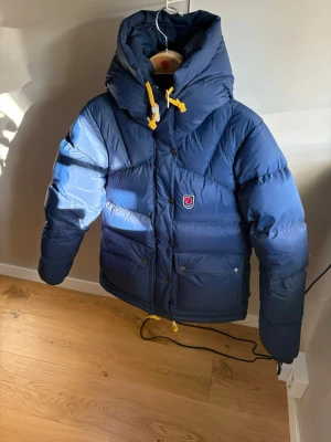 Blå dunjacka från Fjällräven - Snygg blå dunjacka från Fjällräven i superfint skick. Den ser helt ny ut och har inga märken eller skador. Modellen är dam i storlek S. Förvaringspåsen som hör till jackan ingår om man vill ha den. Jag möts endast upp, då jag inte vill skicka den med posten eftersom den är dyr, lägg gärna ett bud ett rimligt pris 