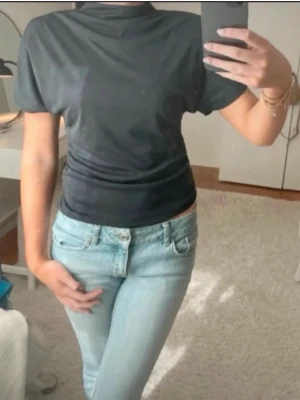 Grå draperad t-shirt med hög hals - En grå, tight t-shirt med hög hals och korta ärmar. Enkel och stilren design som passar perfekt till jeans eller kjol. Tillverkad i mjukt material för en bekväm känsla. Draperad