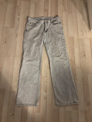 Grå straight fit jeans Woodbird - Snygga grå jeans från Woodbird i straight fit-modell. Jeansen har klassisk femficksdesign, normal midja och dragkedjegylf. Färgen är en tvättad grå med svarta toner, vilket ger en cool vintagekänsla. Perfekta för en avslappnad och trendig stil.