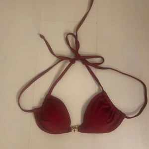Vinröd bikini med gulddetaljer - Snygg vinröd bikini med knyt i nacken och dekorativa guldfärgade detaljer både på överdelen och underdelen. Perfekt för sommaren! Aldrig provad eller använd. Helt ny.