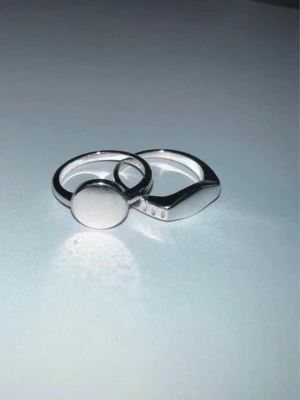 Två silverfärgade chunky ringar - Säljer två stilrena chunky ringar i silverfärgad metall. Ena ringen har en rund, platt topp medan den andra har en kantig, geometrisk form. Perfekta för dig som gillar minimalistiska och moderna accessoarer.