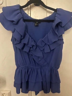 Blå volangtopp från H&M - Supersöt blå topp från H&M med volanger. Använd 2 gånger och säljer den för den inte kommer till användning🌸💐