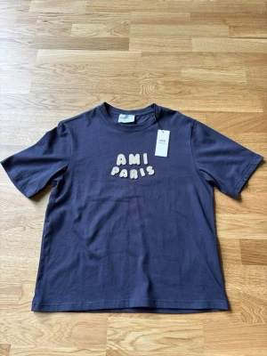 Mörkblå t-shirt från Ami Paris - Snygg mörkblå t-shirt från Ami Paris med broderad text i vitt framtill. Klassisk passform och rund halsringning. Perfekt för dig som gillar stilrena plagg med en twist.