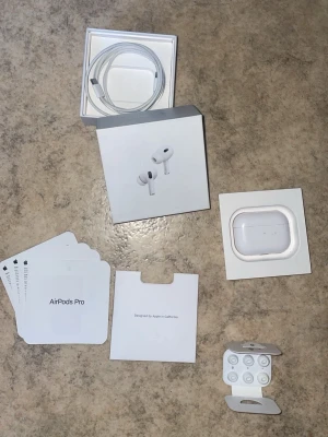 Apple AirPods Pro (2:a gen) med tillbehör  - Säljer ett par vita Apple AirPods Pro (2:a generationen) med trådlöst laddningsetui, extra silikonpluggar och originalförpackning. Allt som behövs för att lyssna trådlöst med grym ljudkvalitet och brusreducering. Lightning till USB-C kabel och manualer medföljer.