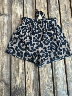Leopardmönstrade shorts med knyt - Säljer ett par leopardmönstrade shorts i beige/brun och svart med hög midja och bred resår. Shortsen har ett snyggt knytband i midjan och är tillverkade i ett mjukt, lätt tyg som passar perfekt till varma dagar.